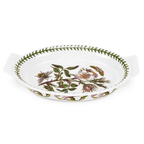 A white oval ceramic baking dish with side handles, decorated with a vintage botanical floral pattern featuring green leaves, pink flowers, and a bee, on a white background.