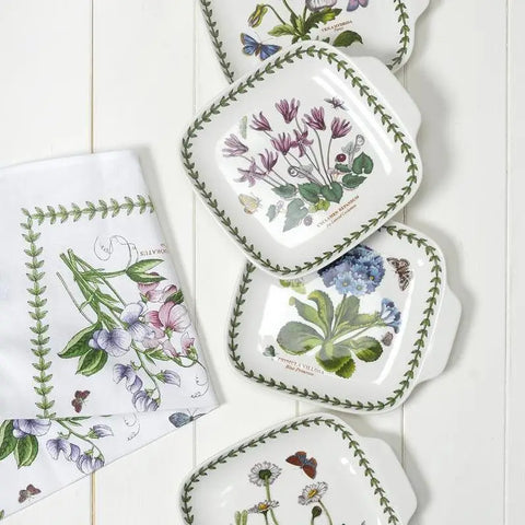 Set of square plates with botanical designs on a white wooden surface