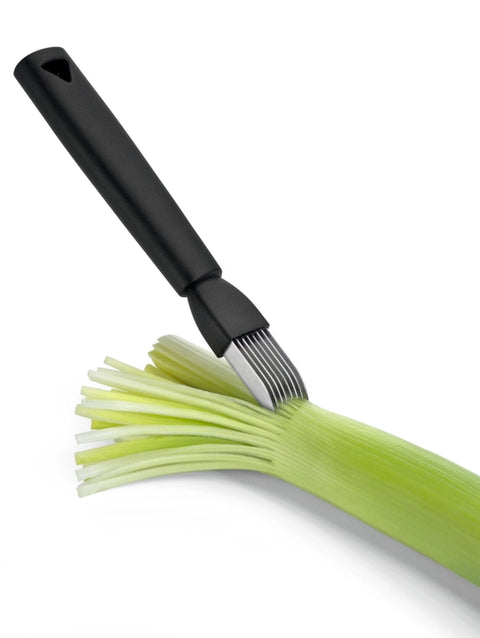 A kitchen utensil with a matte black handle and silver metal tines, shown slicing a green leek on a clean white background.