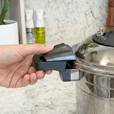 A hand unlocking a pressure cooker pot handle with a kitchen counter in the background