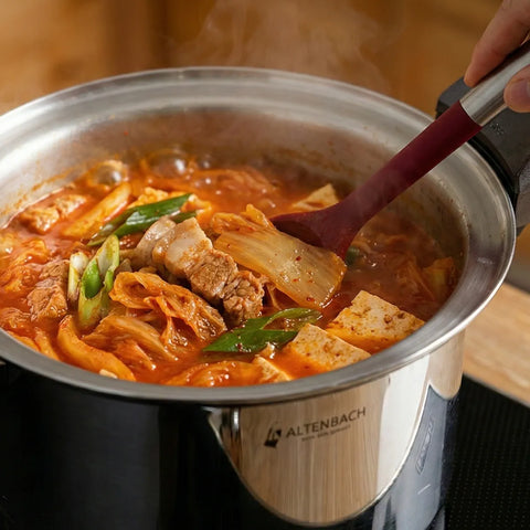Stirring a pot of hot kimchi stew with a red spoon, featuring the cookware brand 'Altenbach'.