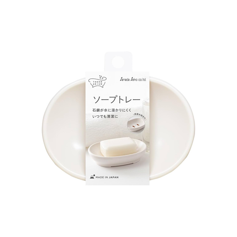 An oval soap dish in a matte off-white plastic finish, shown with its original white paper packaging label featuring Japanese text.