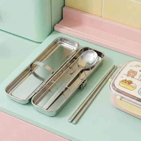 Metal lunch box with cutlery set on a pastel green surface