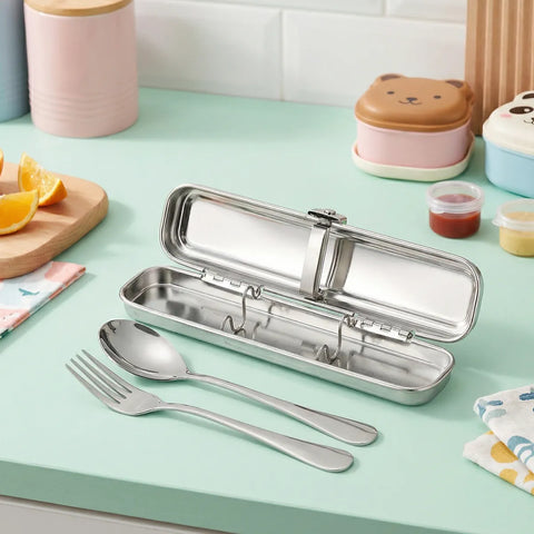 Stainless steel cutlery set in a case on a light green surface with food containers in the background.