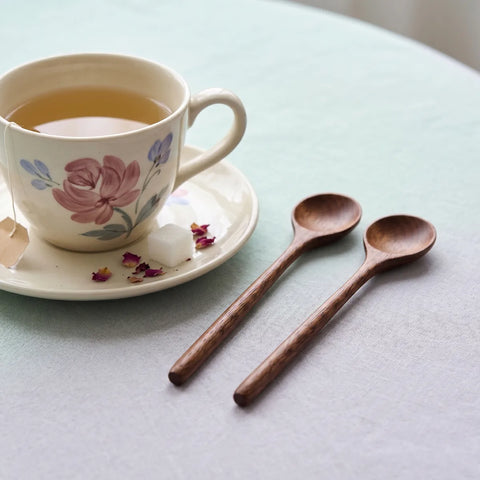 Teacup with floral design on a saucer, accompanied by two wooden spoons on a light surface.