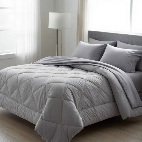 Gray comforter on a bed in a bedroom setting with a lamp and window.