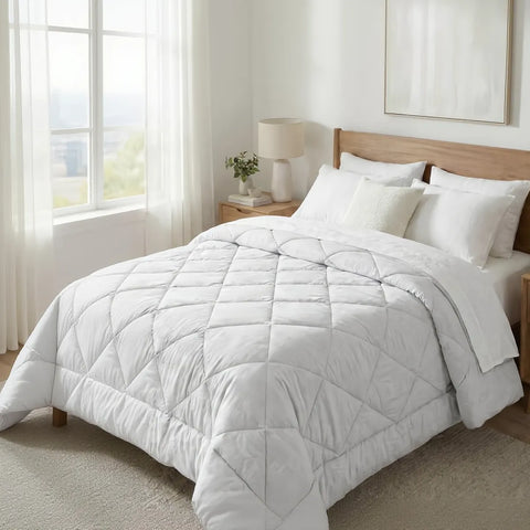 White comforter on a bed in a bright bedroom with large windows.