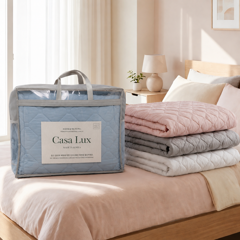 Folded Mattress Pads stacked on a bed next to a 'Casa Lux' packaging box.