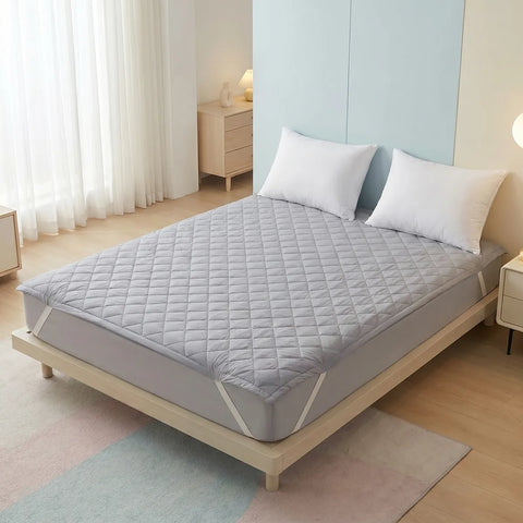 Gray mattress protector on a bed in a bedroom setting with light decor