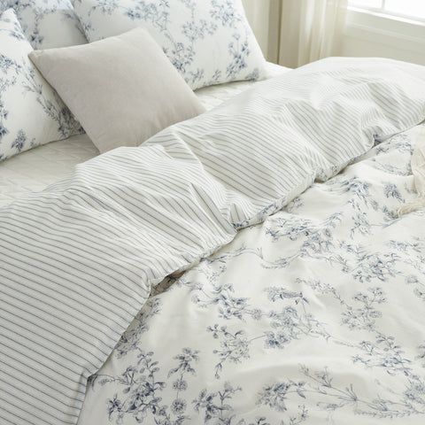 Floral and striped bedding set on a bed with pillows.