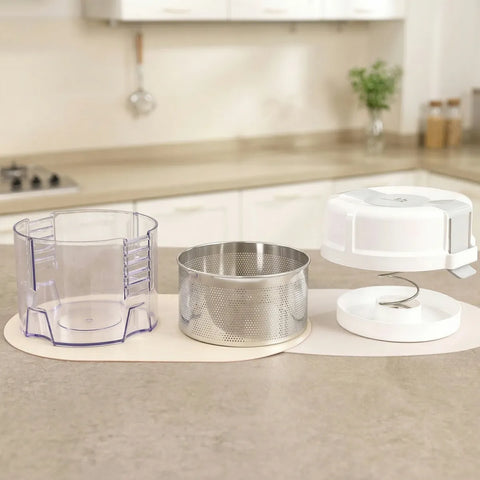 Kitchen countertop with a clear plastic container, metal strainer, and white lid on a beige surface.