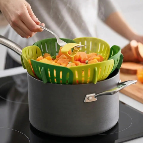 Person using a green kitchen steamer to transfer vegetables from a pot on a stove.