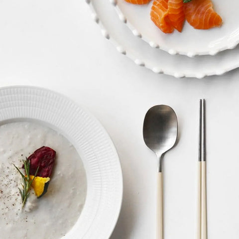 Two plates with food, a spoon, and chopsticks on a white surface