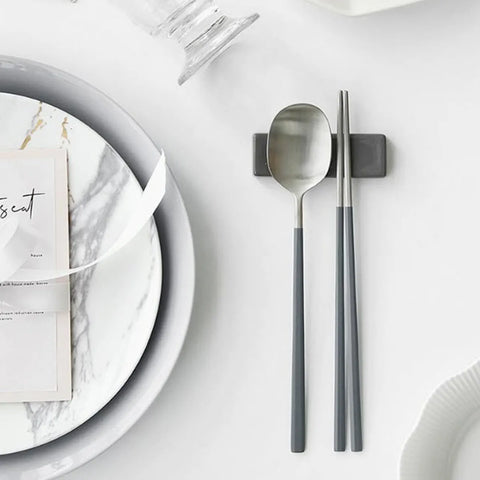 Silver spoon and chopsticks on a marble plate with a card on a white surface