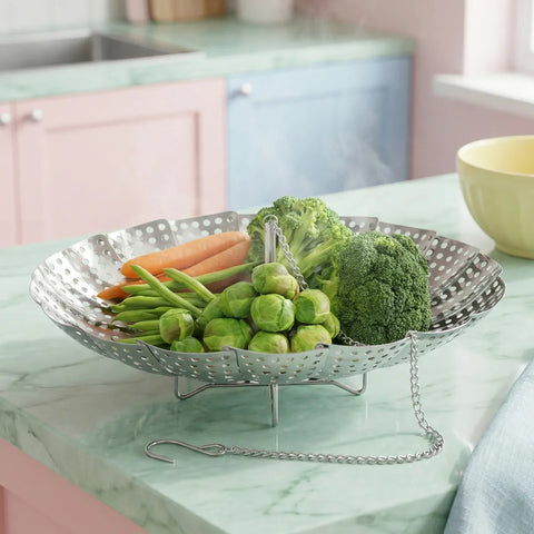 Vegetable steamer basket with carrots, broccoli, and green beans on a kitchen counter.