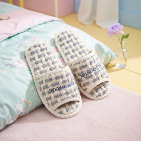 Pair of checkered slippers on a bed with a colorful pillow and flowers in the background