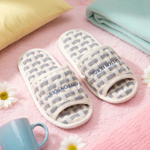 Pair of striped slippers on a pink surface with a mug and flowers.