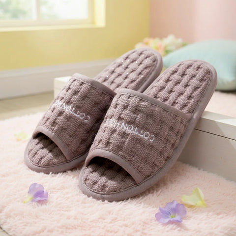 Pair of brown textured slippers on a light pink surface with flowers around.