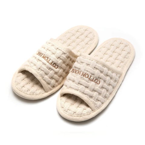 Pair of beige slippers with textured surface and 'Cotton House' branding on a white background