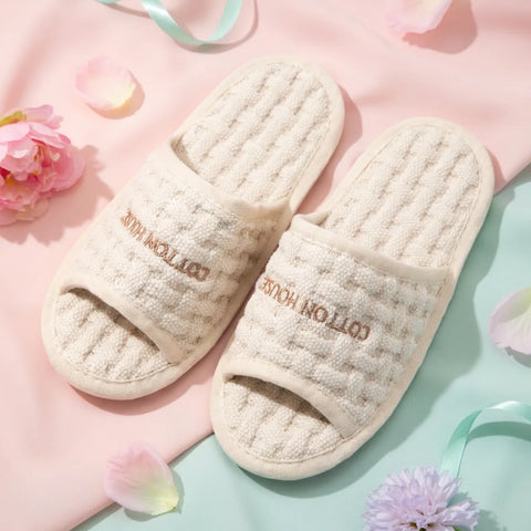 Pair of beige slippers with 'Cotton House' branding on a pink and green background with flowers.