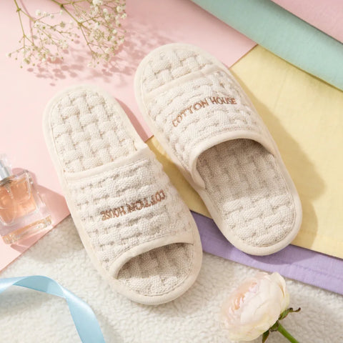 Ivory slippers with 'Cotton House' branding on a soft pastel background.