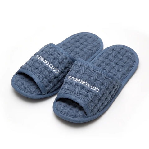 Pair of blue textured slippers with 'Cotton House' branding on a white background