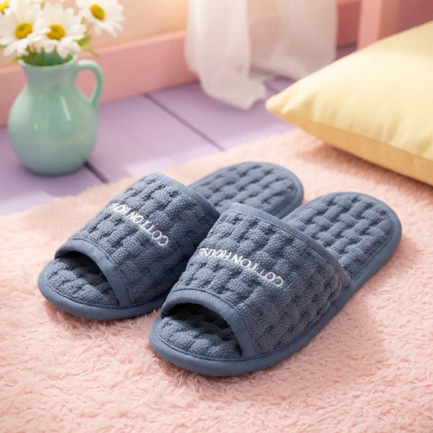 Blue slippers with 'Cotton House' branding on a pink surface, with a vase of flowers in the background.