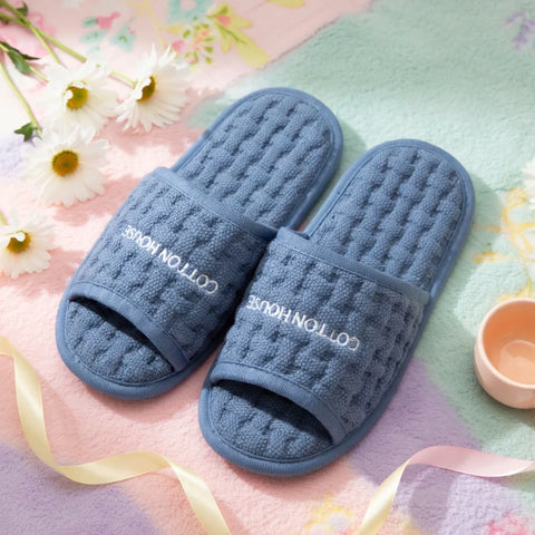 Pair of blue slippers with 'Cotton House' branding on a floral background