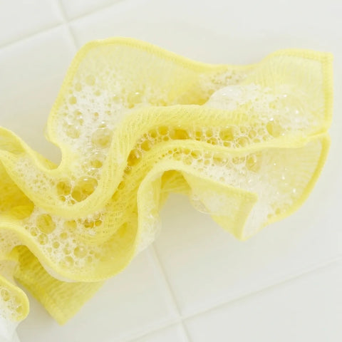 Yellow sponge cloth with foam on a white tiled background