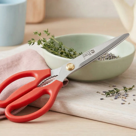 Pair of red kitchen scissors resting on a bowl of herbs on top of a wooden cutting board