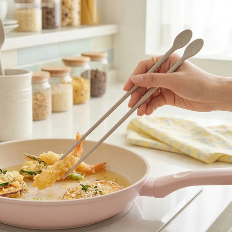 Person using chopsticks to pick up food from a pan on a kitchen counter.
