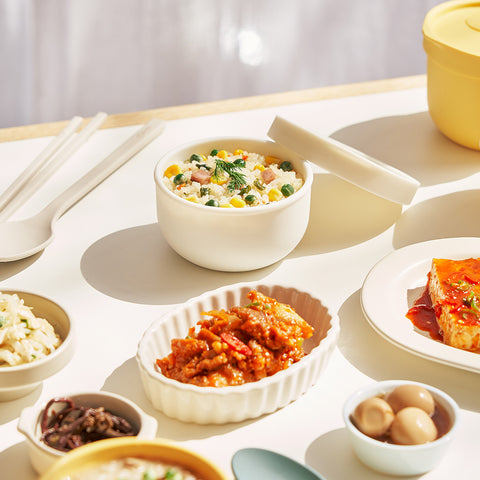 Assorted dishes with a bowl of rice, side dishes and utensils on a white table