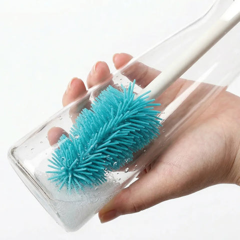 Hand holding a glass with a blue cleaning brush inside, against a white background