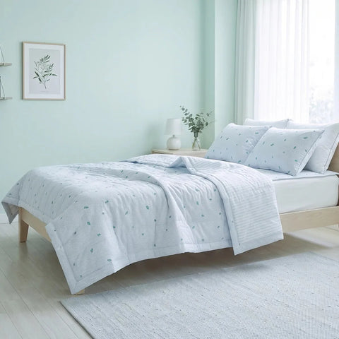 A light blue and white bedding set with a small leaf pattern, styled on a light wood bed frame in a bright, pale green bedroom.
