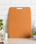 Brown cutting board on a kitchen counter with a white tiled wall background