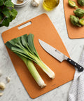 Brown cutting board with leeks and a knife on a marble countertop.