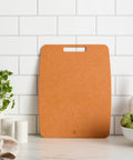 Brown cutting board on a kitchen counter with a white tiled wall background