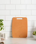 Brown cutting board on a kitchen counter with a white tiled wall background
