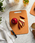 Brown cutting board with sliced apples, a knife, and bread on a marble surface.