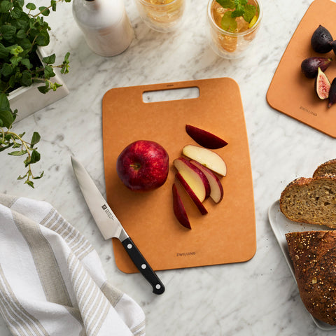 Brown cutting board with sliced apples, a knife, and bread on a marble surface.