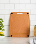 Brown cutting board on a kitchen counter with a white tiled wall background