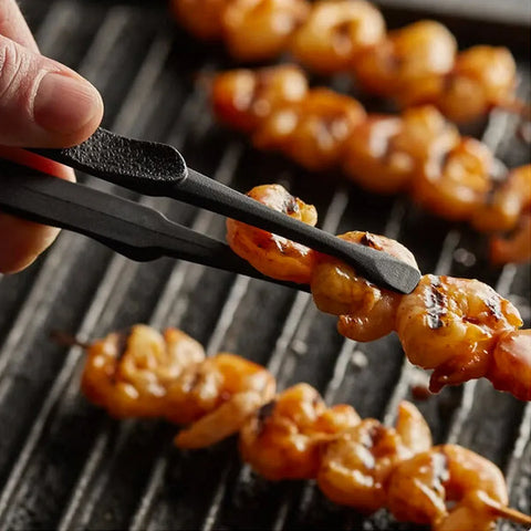 Grilled shrimp skewers being held by tongs over a grill