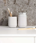 White toothbrush holder with toothbrushes and a white soap dispenser on a gray countertop.
