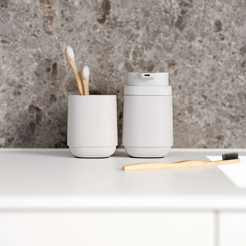 White toothbrush holder with toothbrushes and a white soap dispenser on a gray countertop.