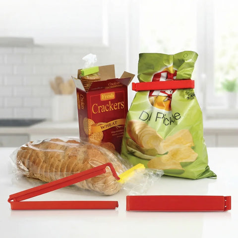 Red bag clips used on a bag of chips and a box of crackers on a kitchen counter.