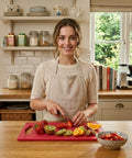 Woman in a kitchen preparing fruits on a red cutting board.