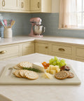 Kitchen counter with a cheeseboard, crackers, and fruit on a white countertop.