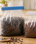 Two bags of coffee beans on a wooden surface with a clear plastic bag containing coffee beans.