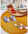 Decorative cutlery set on a yellow placemat with a floral-patterned bowl in the background.