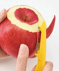 Hand holding a red apple with a yellow peeler cutting into it on a white background